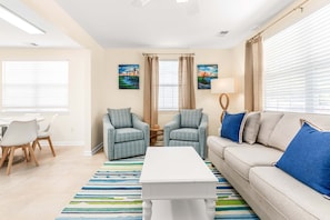 A living room with a beige sofa, two plaid armchairs, a white coffee table, and a striped rug. - Bowline Bungalow Tybee Vacation Rentals (Tybee Island)