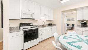 A modern kitchen with white cabinets, a stove, microwave, and a dining area with a table and chairs. - Bowline Bungalow Tybee Vacation Rentals (Tybee Island)