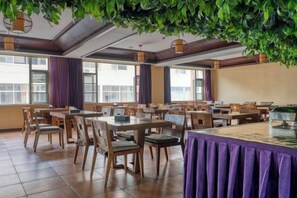 A dining area with tables and chairs, large windows, and a ceiling with hanging plants. - Bianchui Hotel (Yingjiang)