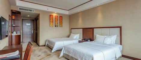 A hotel room with two beds, a desk, and a television.