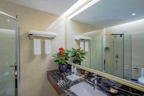 Une salle de bain moderne avec un grand miroir, un comptoir en marbre et une cabine de douche en verre.