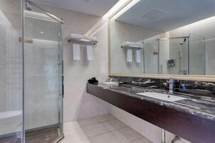 Un baño moderno con cabina de ducha de vidrio, encimera de mármol oscuro y un espejo grande.