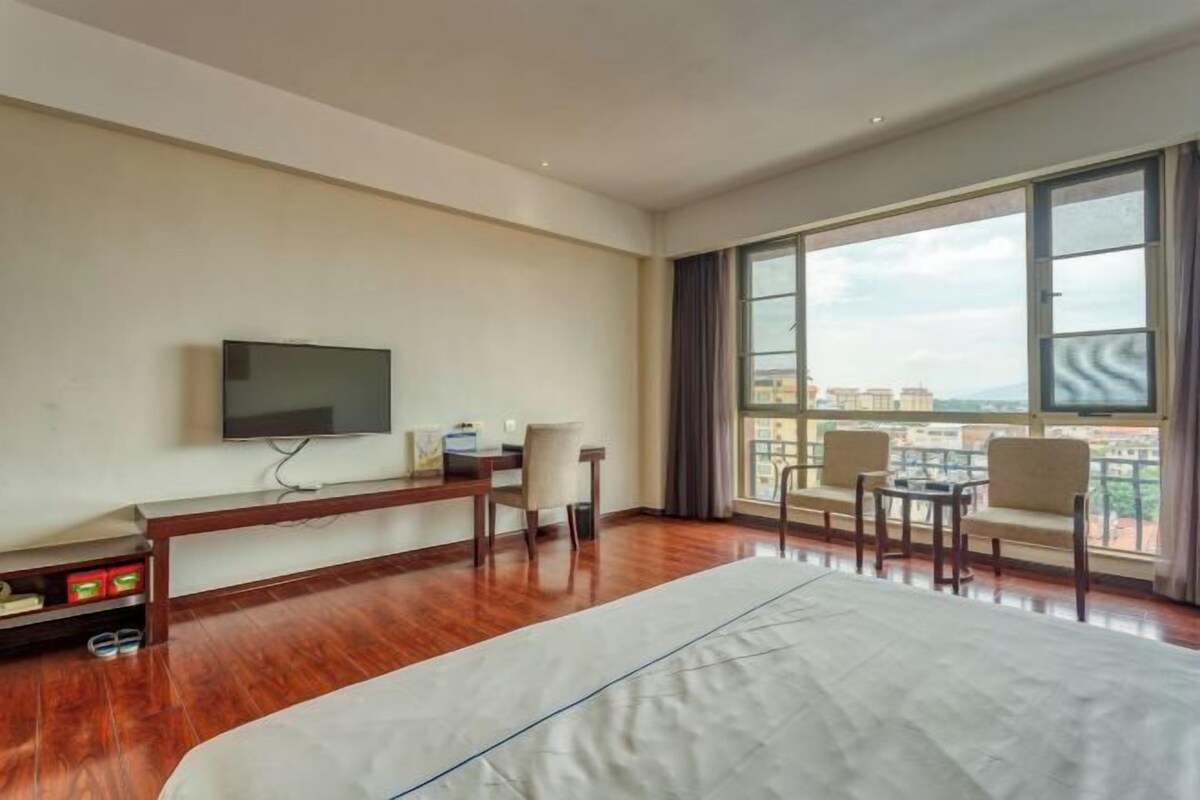 Une chambre d’hôtel avec un grand lit, une télévision, un bureau avec des chaises et un balcon avec vue.