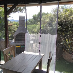 A covered outdoor area with a stone-built barbecue grill, wooden table, and chairs.