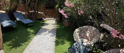 A garden with a gravel path, green lawn, and outdoor seating area with chairs and a table.