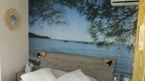 Een slaapkamer met een bed, kussens, een nachtkastje, een wandairconditioner en een muurschildering van een strand.