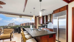 A modern kitchen with a large island, stainless steel appliances, and a view of the cityscape. - Hale Kai Pampered Ko Olina Villa (Kapolei)