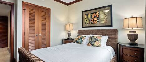 A neatly arranged bedroom with a large bed, two bedside tables with lamps, a wicker chair, and a ceiling fan.
