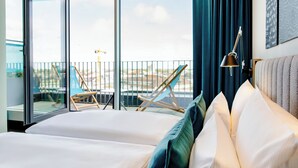 A hotel room with a large bed, a desk lamp, and a view of the city through a glass door. - Motel One Karlsruhe (Karlsruhe)
