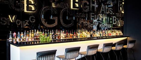 Una zona de bar con una barra alargada que exhibe varias botellas, y tres taburetes con rayas.