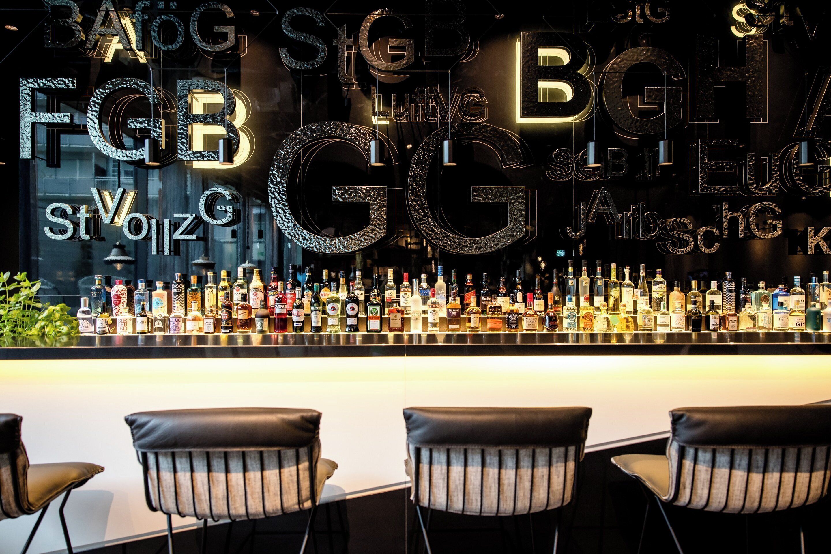 Un bar con una variedad de botellas de licor y un letrero de neón. Hay cuatro taburetes de bar frente a la barra.