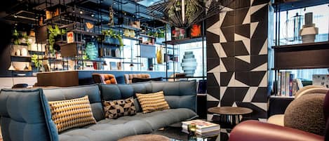 Un área de descanso moderna con un sofá azul, sillones de cuero y una mesa de centro. Se observan estanterías con libros y objetos decorativos.
