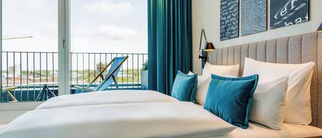 Habitación de hotel con una cama grande, almohadas azules, cabecera y una obra de arte en la pared.