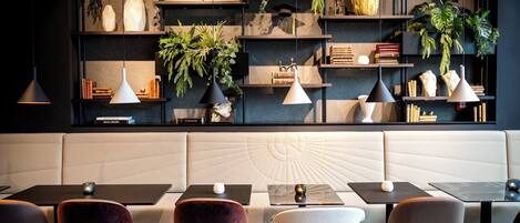 A modern interior with a seating area, tables, and shelves with plants and books.