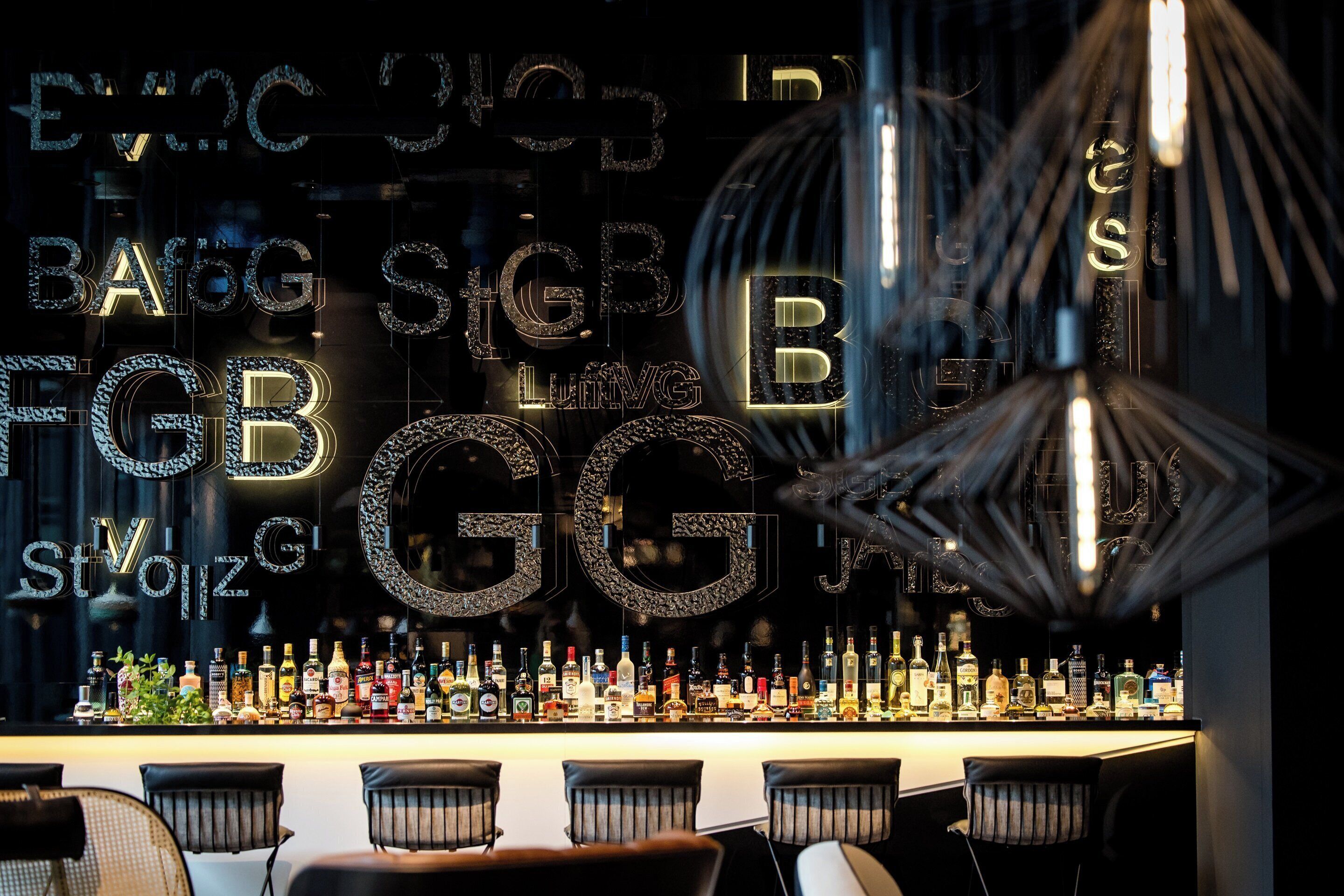 A bar area with a variety of liquor bottles and a decorative wall with illuminated letters.