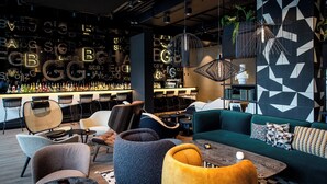 A modern bar area with a variety of seating options, including sofas and chairs, and a bar stocked with bottles. - Motel One Karlsruhe (Karlsruhe)