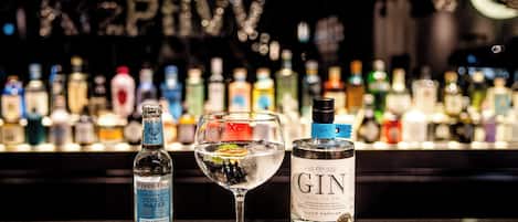 A bar setting with a glass of white wine, a bottle of gin, and a bottle of tonic water on a counter.