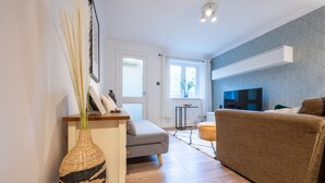 Een moderne woonkamer met een grijze bank, een bruine bank, een gevlochten vaas en een flatscreen televisie aan de muur.