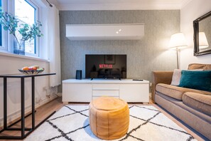 A modern living room with a flat-screen TV, a sofa, a coffee table, and a patterned rug.