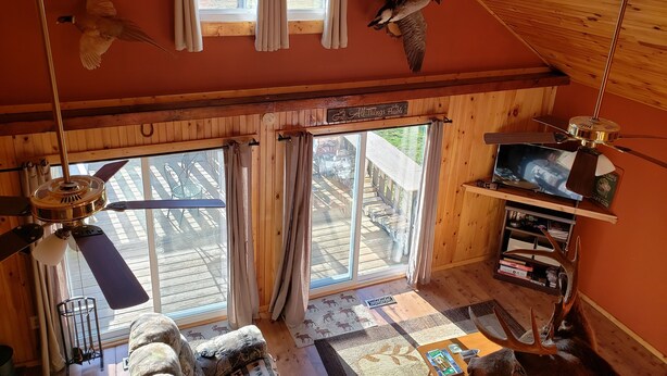 A cozy cabin with a wooden interior, a ceiling fan, a mounted television, and a large window with curtains.