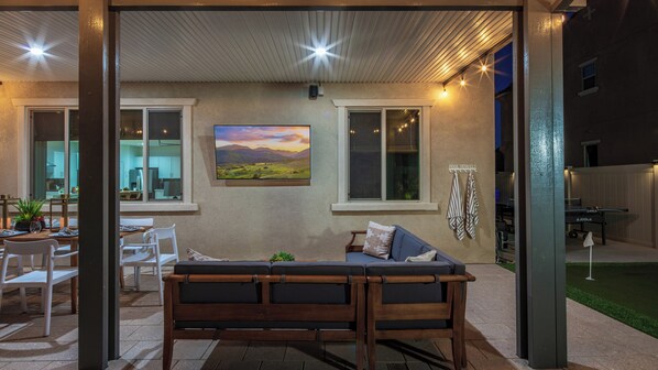 An outdoor patio area with a wooden bench, a dining table with chairs, and a painting of a landscape. - 2 Mi. To Coachella Festival - Pool, Spa, Gameroom (Coachella)