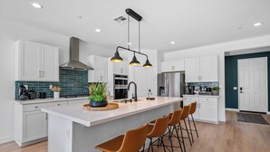 A modern kitchen with white cabinets, a large island with bar stools, and pendant lighting. - 2 Mi. To Coachella Festival - Pool, Spa, Gameroom (Coachella)