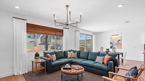 A modern living room with a sectional sofa, a round ottoman, a wooden side table, and a chandelier. - 2 Mi. To Coachella Festival - Pool, Spa, Gameroom (Coachella)