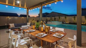 An outdoor dining area with a pool, wooden tables, and chairs, under a covered roof with string lights. - 2 Mi. To Coachella Festival - Pool, Spa, Gameroom (Coachella)
