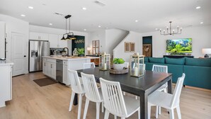 A modern kitchen with white cabinets, a stainless steel refrigerator, and a dining area with white chairs. - 2 Mi. To Coachella Festival - Pool, Spa, Gameroom (Coachella)