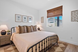 A bedroom with a bed, bedside tables, lamps, framed pictures, and a window with a view. - 2 Mi. To Coachella Festival - Pool, Spa, Gameroom (Coachella)