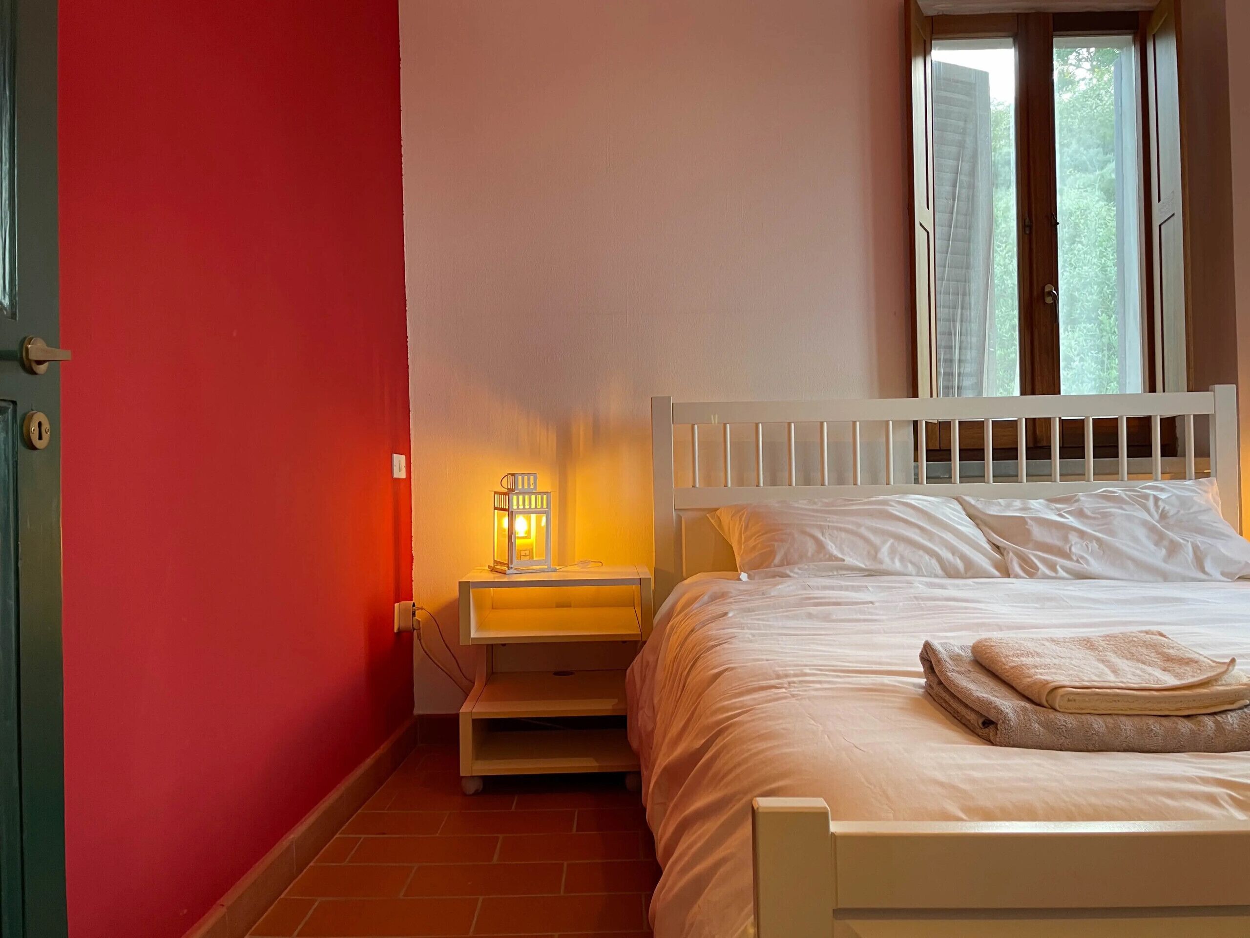 Une chambre à coucher avec un lit, une table de chevet, une lampe fixée au mur et une fenêtre avec des rideaux.