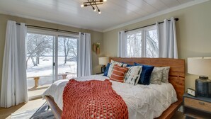 A bedroom with a wooden bed, white bedding, a red knitted blanket, and a nightstand with a lamp. - Home Rental on Detroit Lake: Dock, Game Room! (Detroit Lakes)