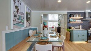 A modern dining area with a glass table, teal cabinetry, and a view of a pool. - Home Rental on Detroit Lake: Dock, Game Room! (Detroit Lakes)