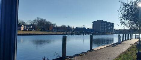 A calm waterfront view with a pathway, a building in the background, and a clear sky.