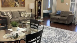 Un salón amplio con una mesa redonda de cristal, dos sofás, una estantería y un cuadro grande.