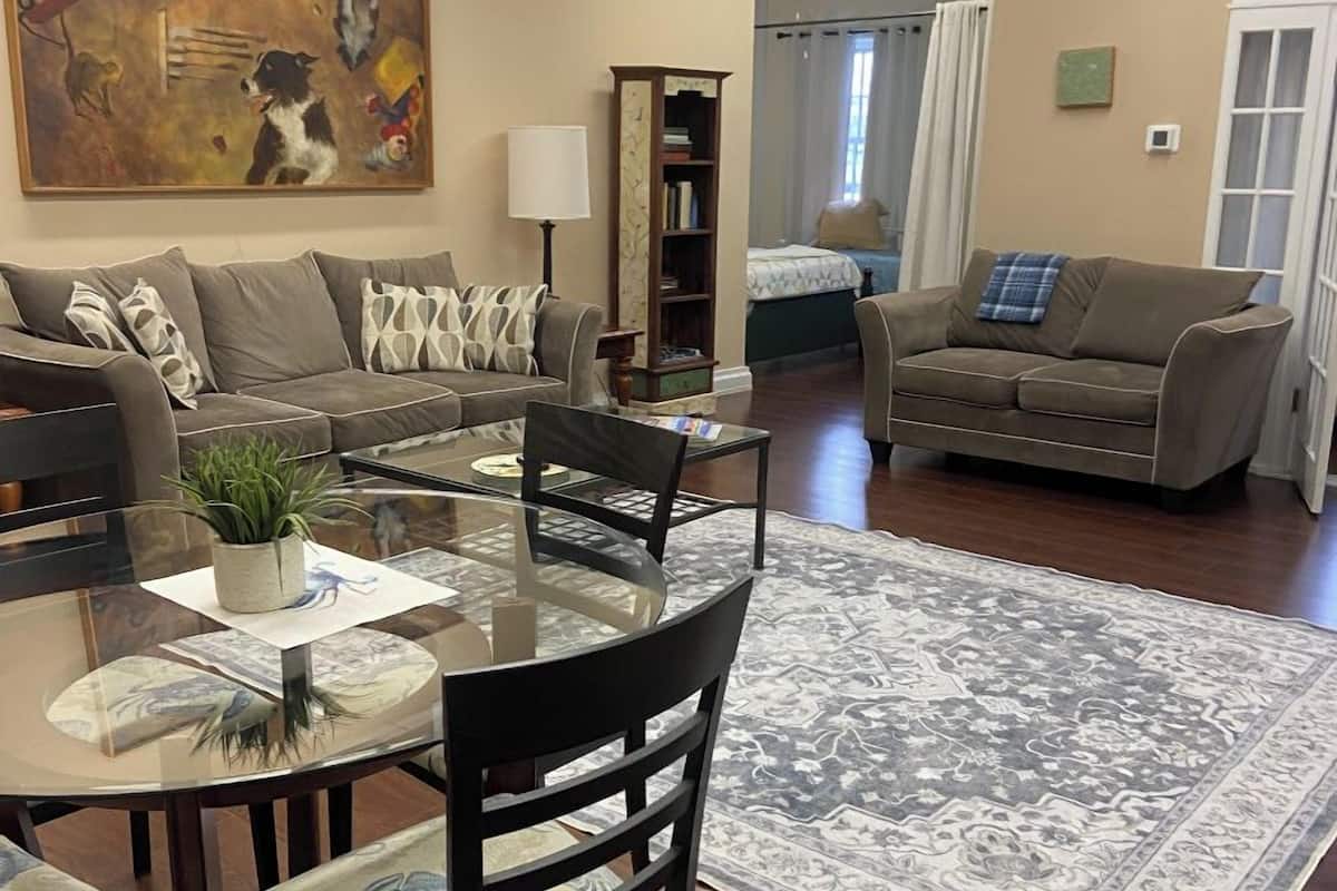 A spacious living area with a round glass table, two sofas, a bookshelf, and a large painting.