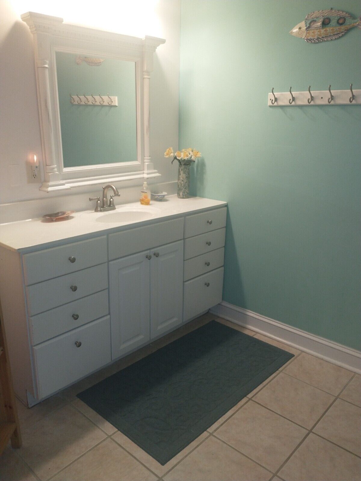A bathroom with a white vanity, a mirror, and a vase with yellow flowers.