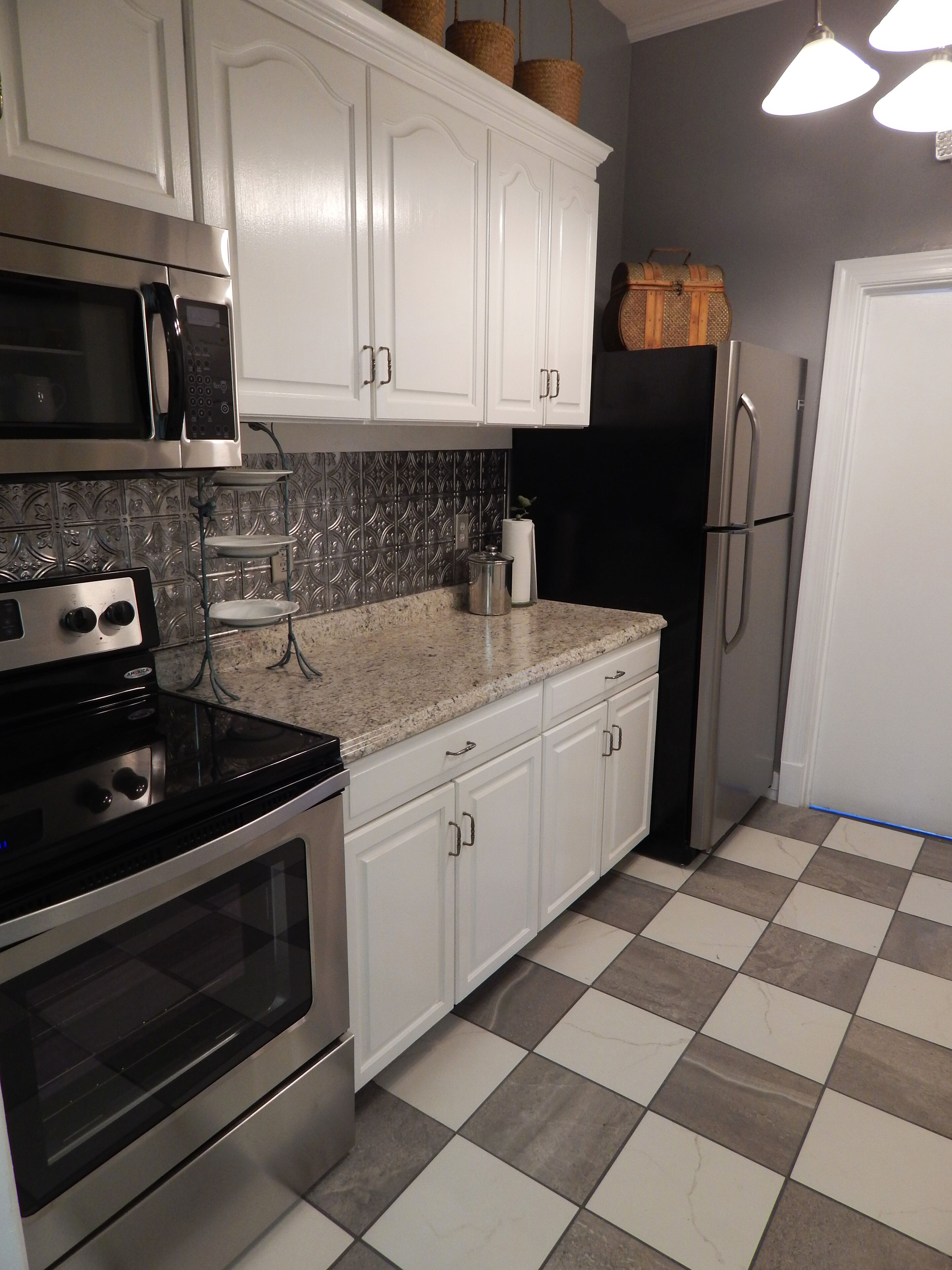 Una cocina con gabinetes blancos, un refrigerador de acero inoxidable, un microondas y una estufa.
