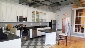 Una cocina con gabinetes blancos, electrodomésticos de acero inoxidable, piso a cuadros y una silla de madera.