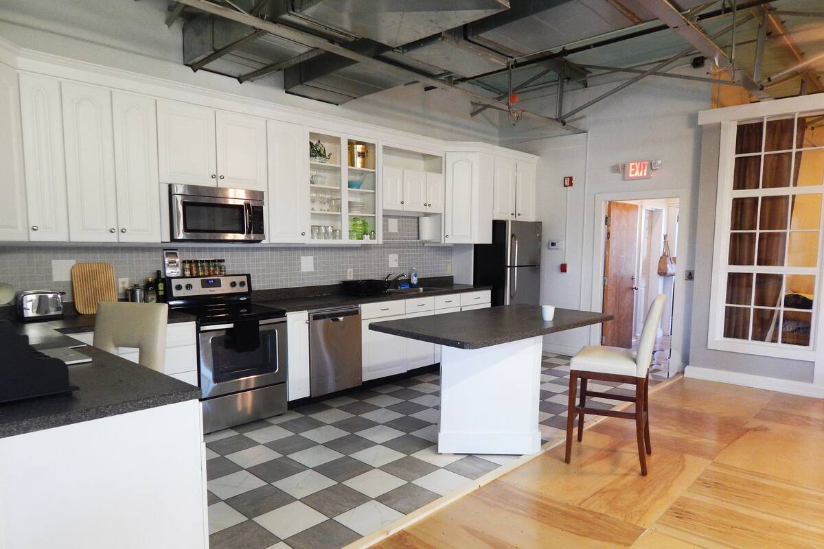 A kitchen with white cabinets, stainless steel appliances, a checkered floor, and a wooden chair.