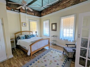 A bedroom with a wooden bed, a ceiling fan, a small table, a chair, and a window with a view. - Salisbury Riverfront Lofts (Salisbury)