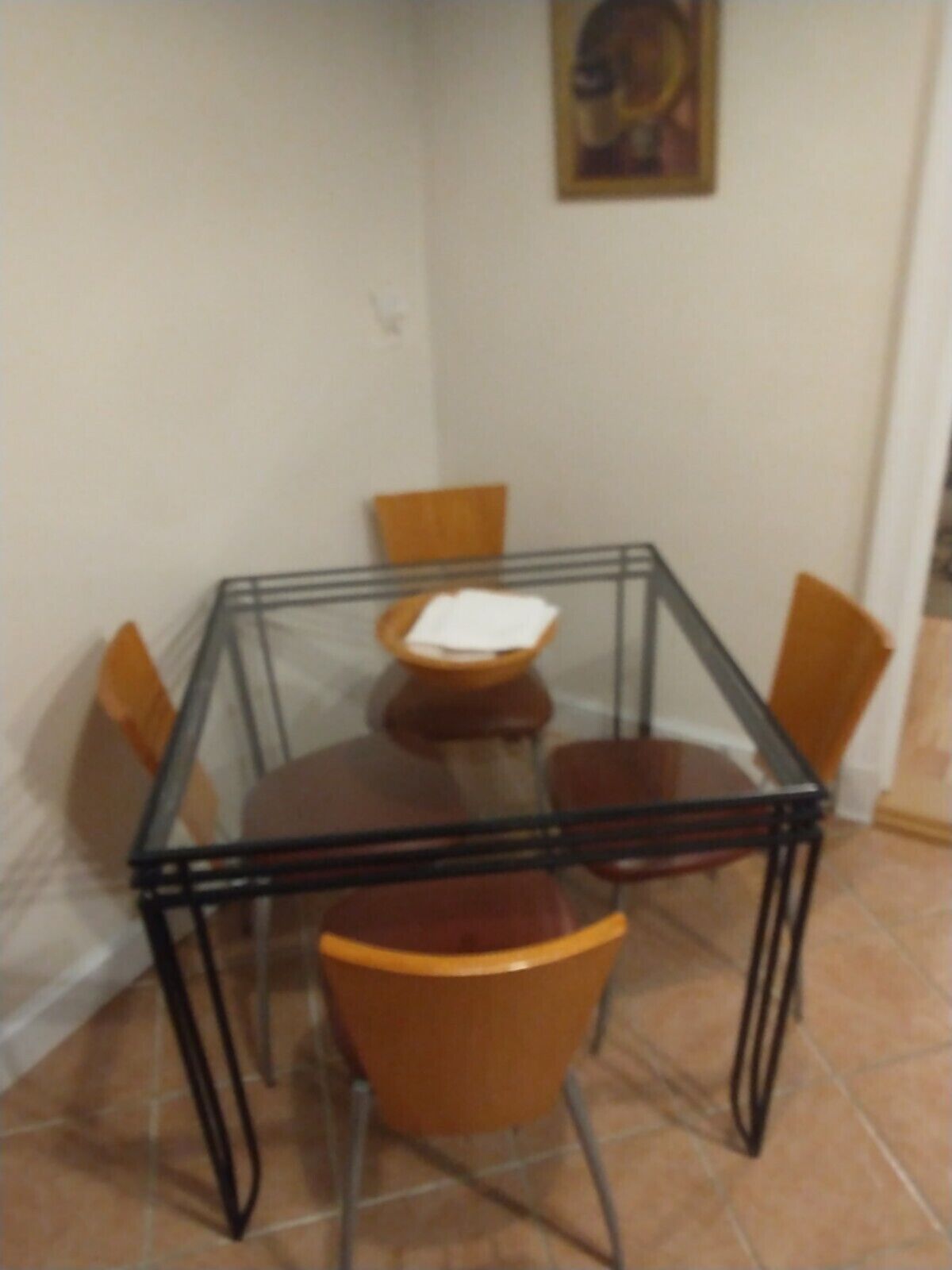 A dining area with a glass-top table surrounded by four wooden chairs.