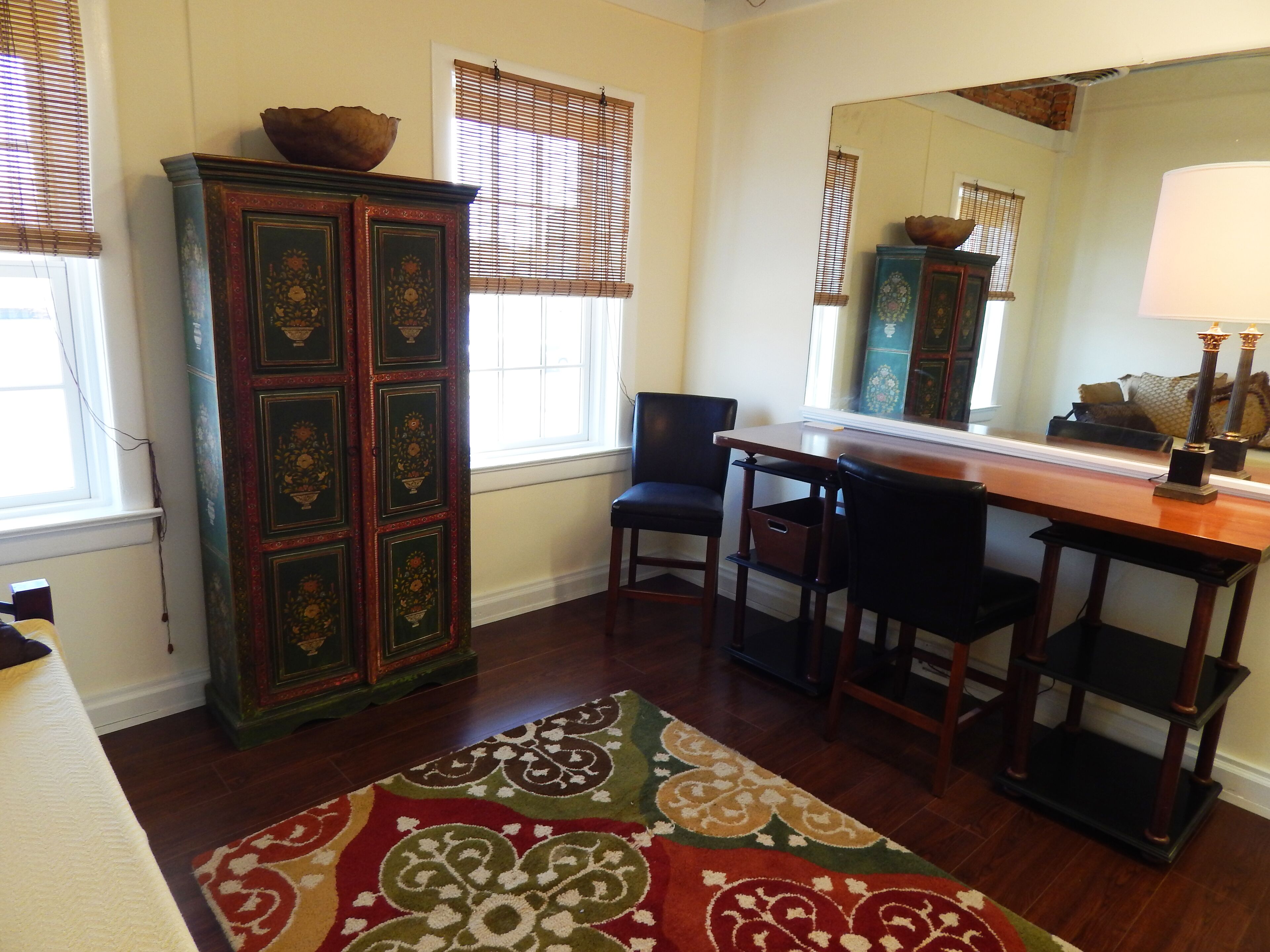 A room with a wooden cabinet, two chairs, a table, and a mirror.