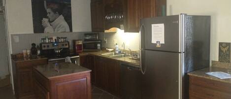 A compact kitchen with wooden cabinets, a stainless steel refrigerator, a microwave, and a sink.