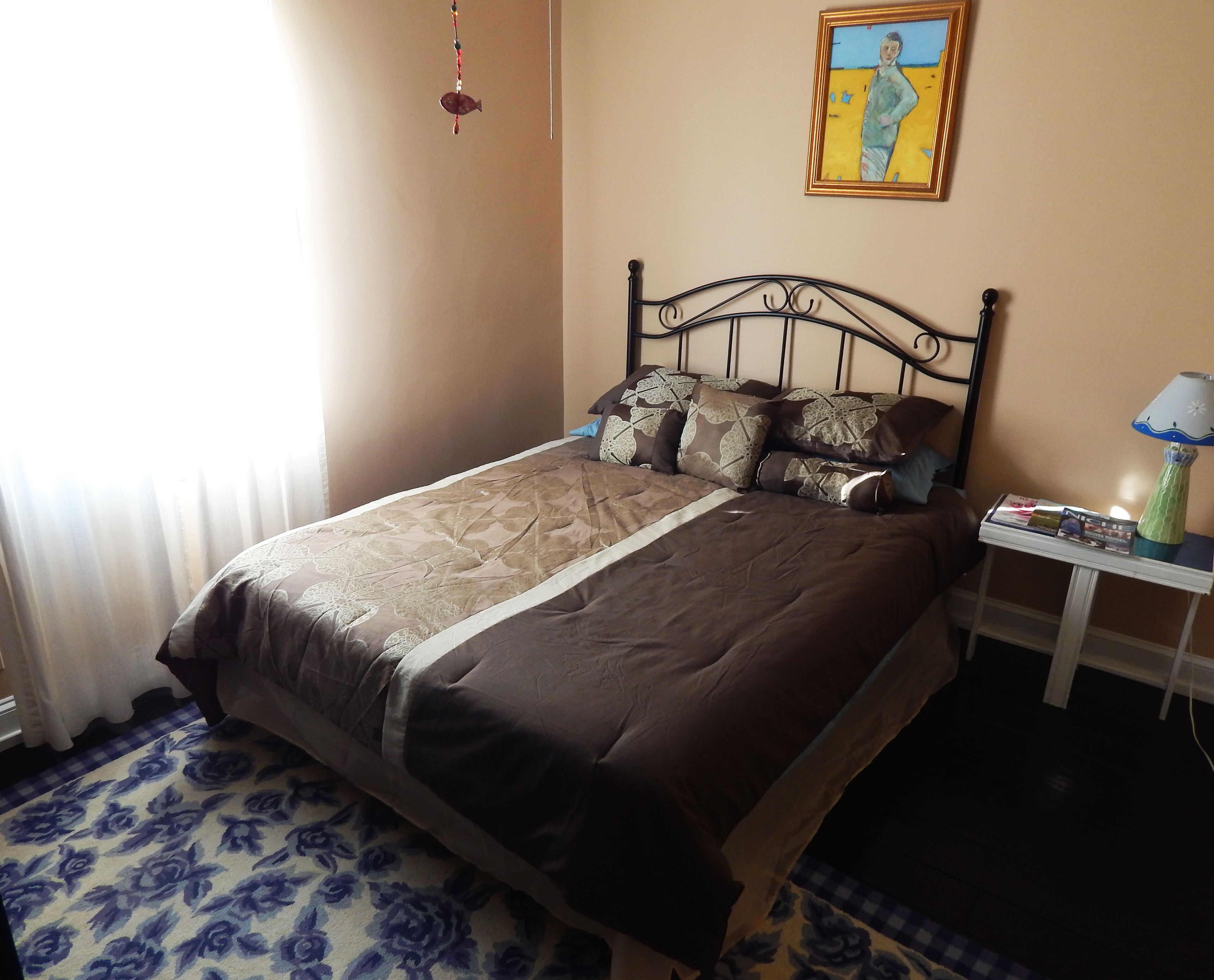 A neatly made bed with a patterned bedspread, a bedside table with a lamp, and a framed painting on the wall.