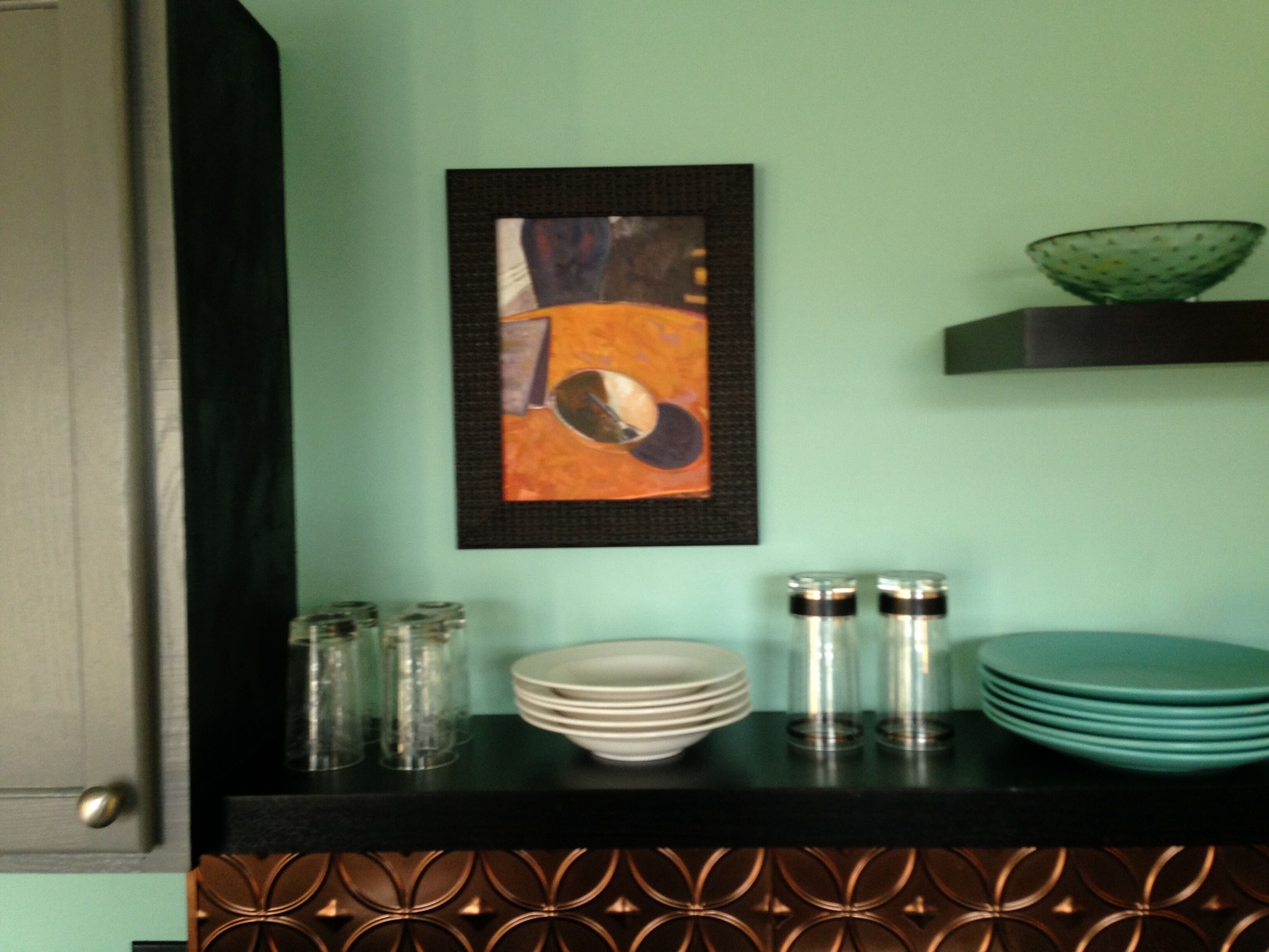 A kitchen counter with a framed abstract painting, stacked plates, and glass containers.