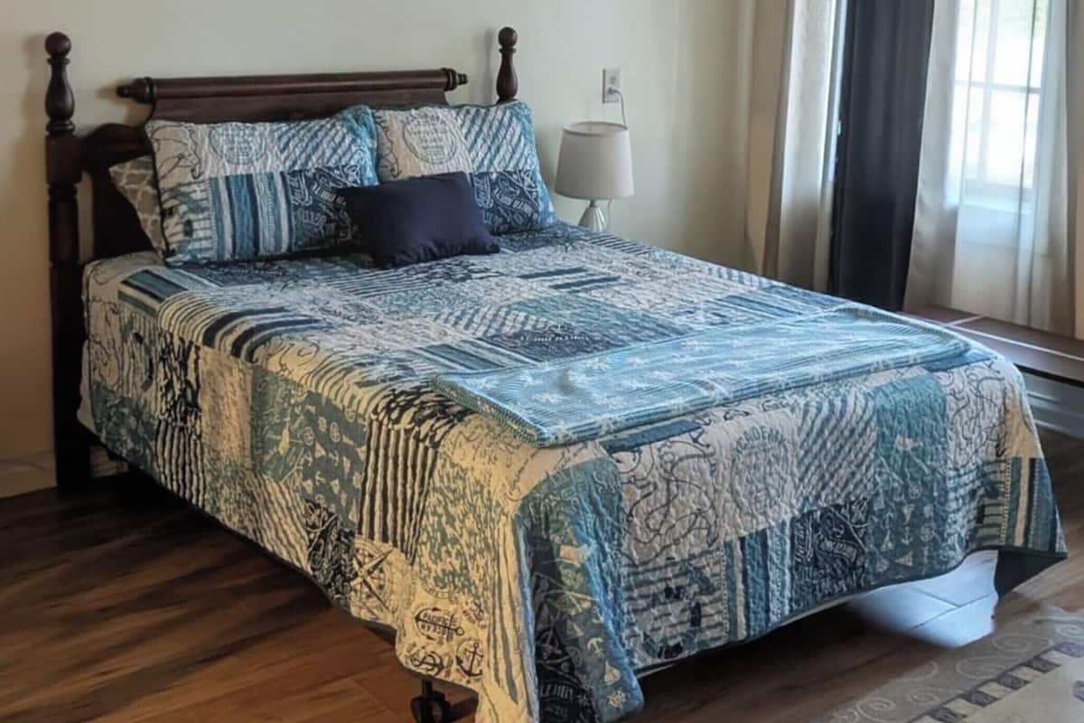 A bedroom with a bed, a nightstand, a lamp, a painting, and a window with curtains.