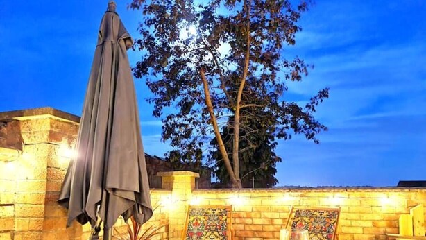 A patio with a table, a glass of red wine, and a brick wall with a tree and an umbrella. - Stylish 3 Bedroom Victorian Villa with hot tub (Lincoln)