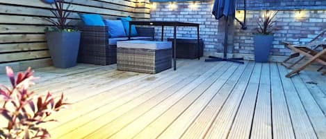 Une terrasse extérieure dotée d'un plancher en bois, de meubles en osier et de plantes en pot.