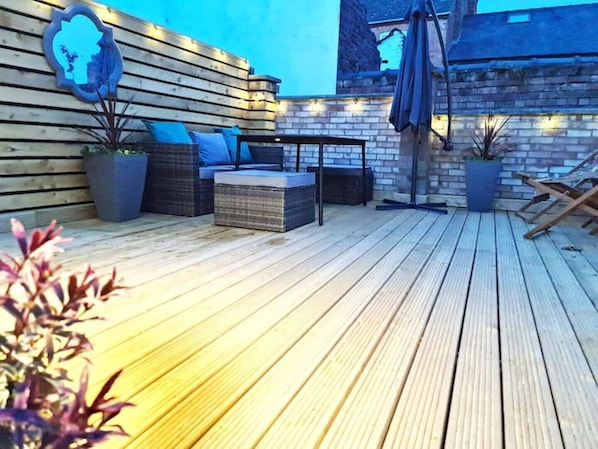 An outdoor patio with wooden flooring, wicker furniture, and potted plants. - Stylish 3 Bedroom Victorian Villa with hot tub (Lincoln)